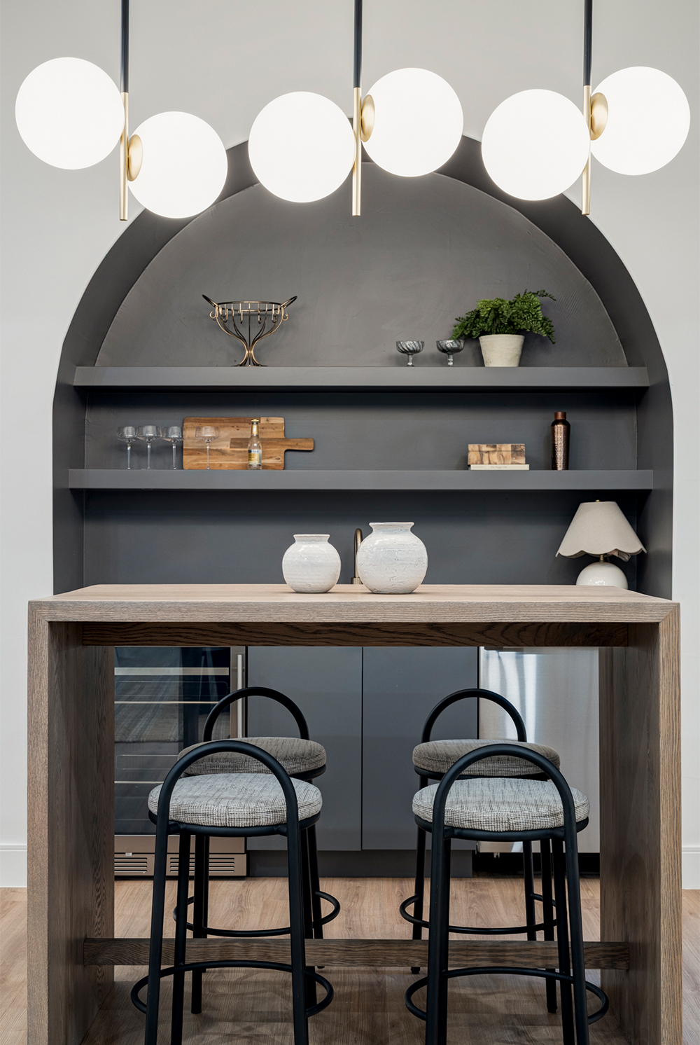 Custom arched wet bar with open shelving, statement lighting, and built-in seating.