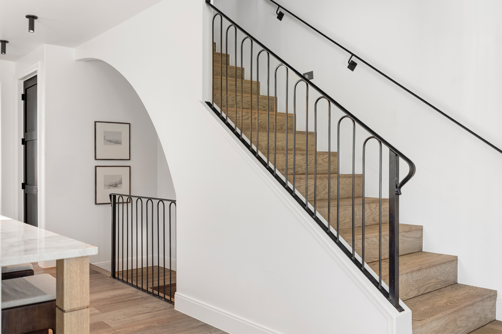 Modern staircase with black railing and warm wood flooring in luxury row home.