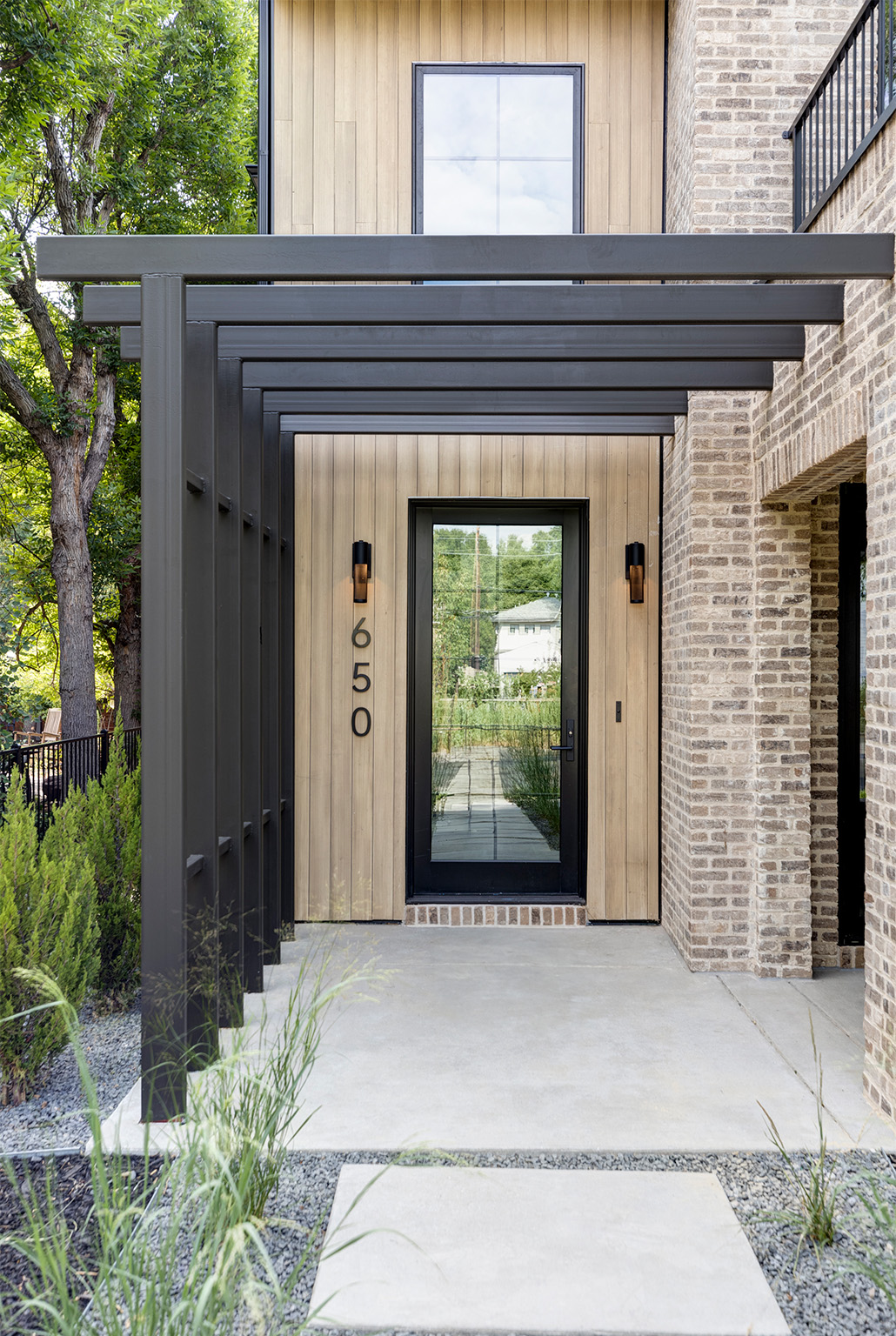 Modern front entry walkway with sleek pergola and natural wood door.
