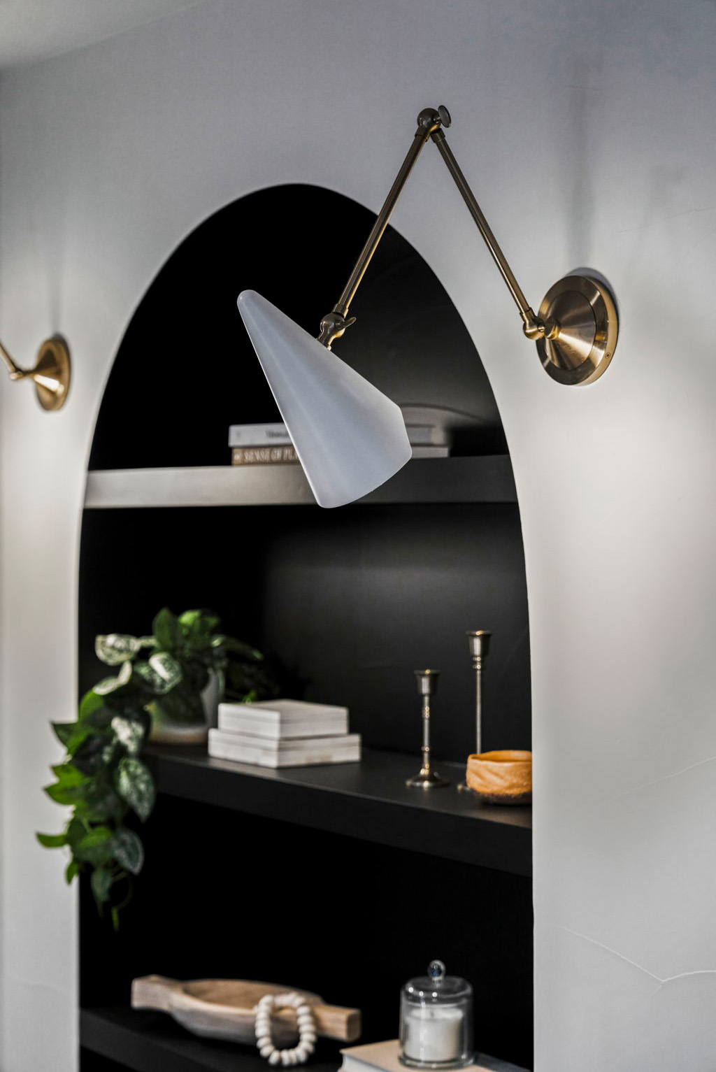 Custom arched built-in shelving nook with modern brass sconce lighting.