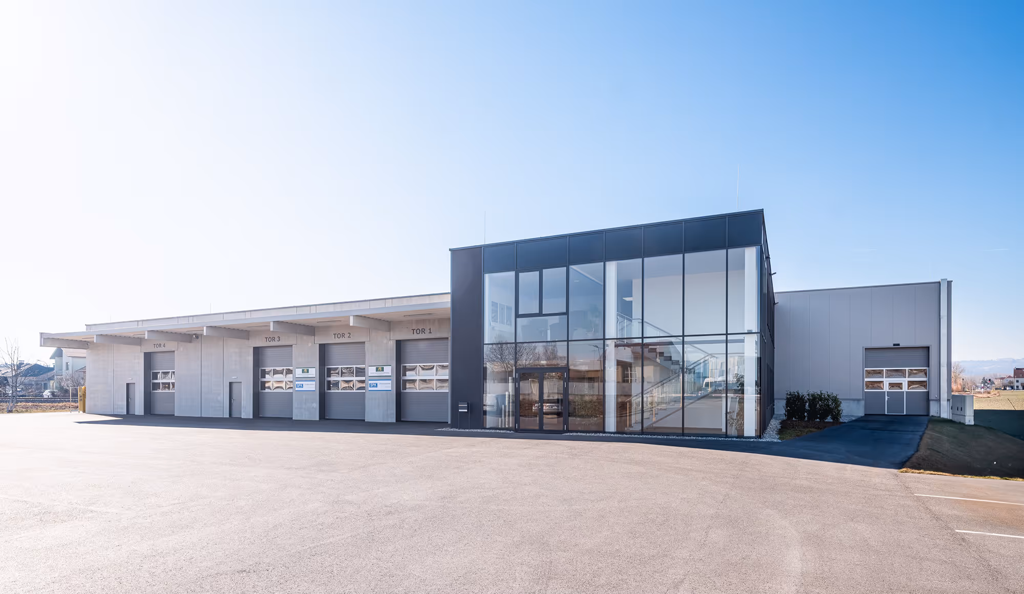 Modernes Industriegebäude der Akustik Buch mit großem Glasfoyer und mehreren Laderampentüren unter strahlend blauem Himmel.