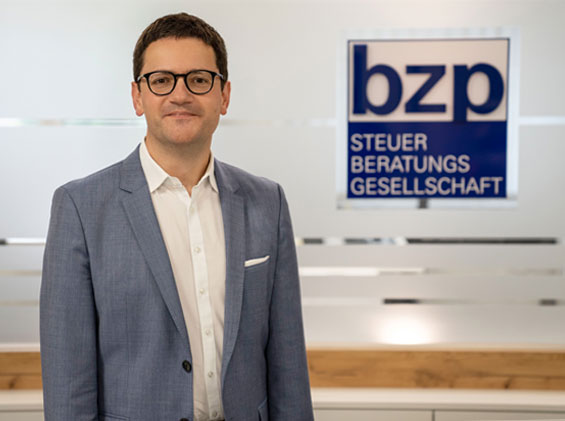 Mann mit Brille vor bzp-Schild, freundlich schauend