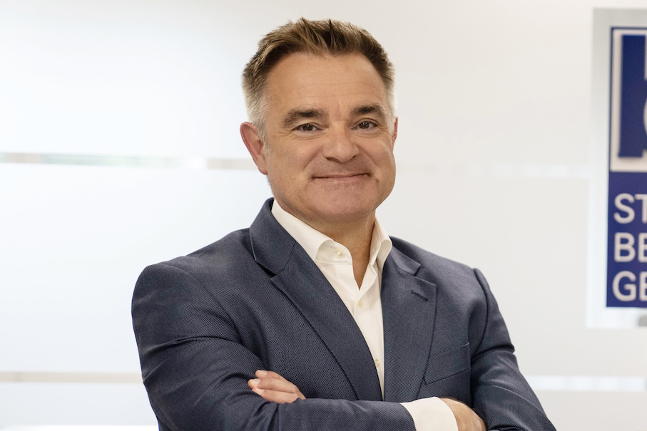 Mann mit verschränkten Armen im grauen Anzug, lächelt