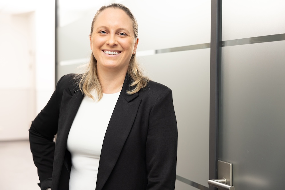 Blonde Frau im Anzug steht vor weißer Wand