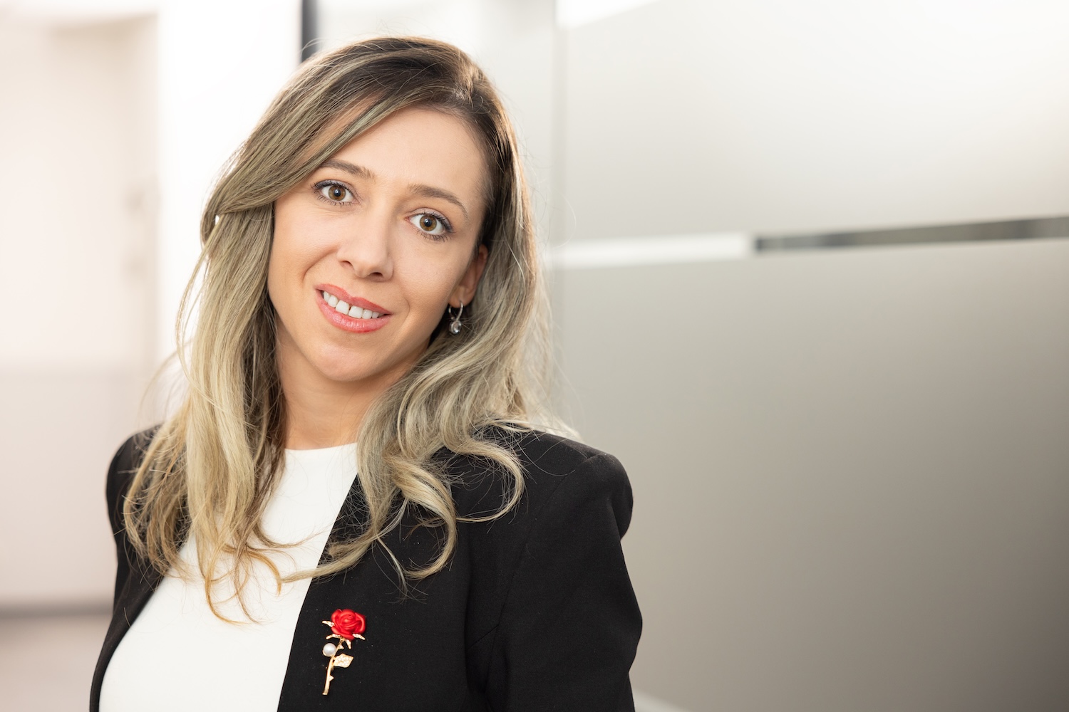 Porträt einer lächelnden Frau mit blondem Haar in Businesskleidung vor neutralem Hintergrund.