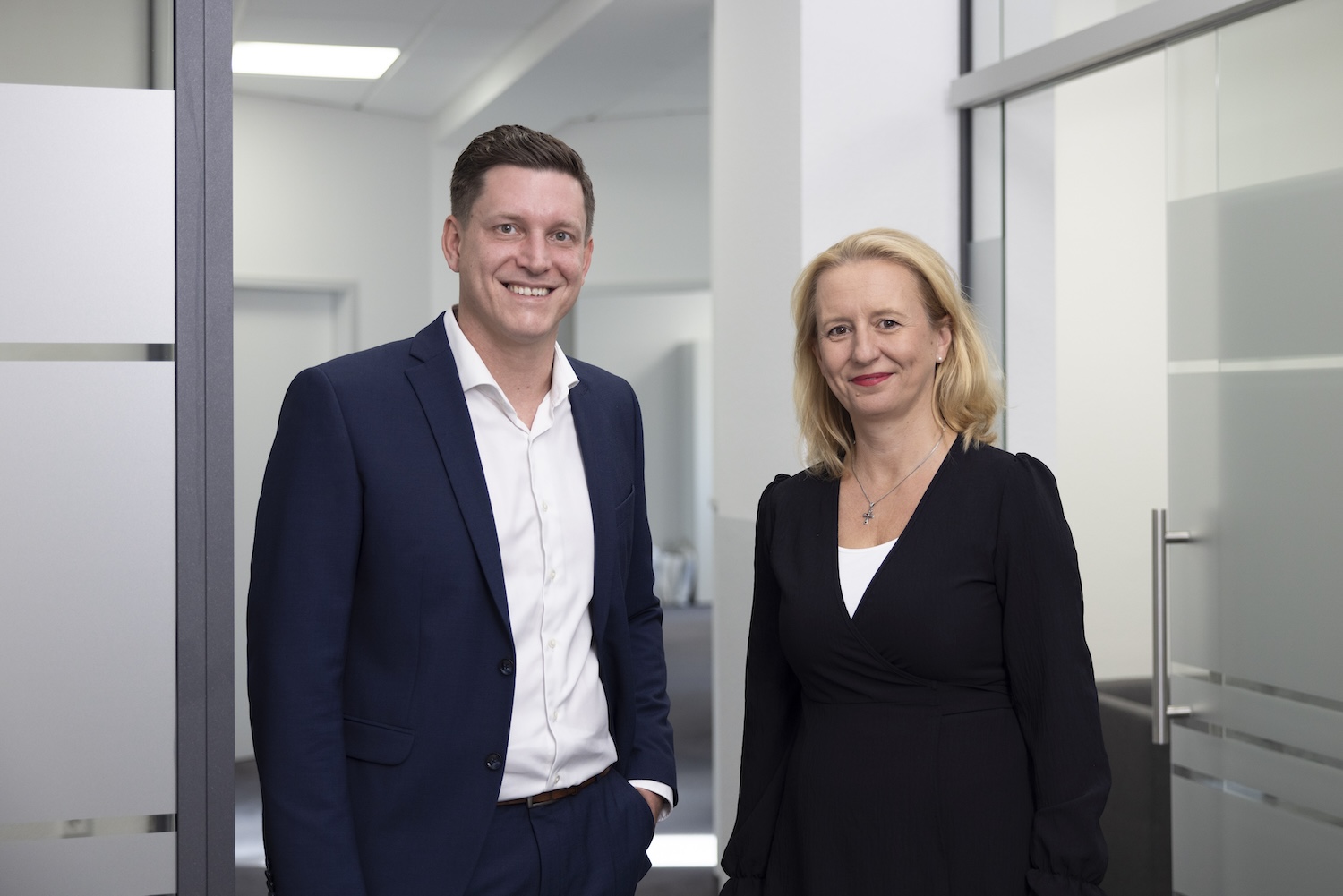 Zwei Personen im Business-Outfit lächeln in die Kamera