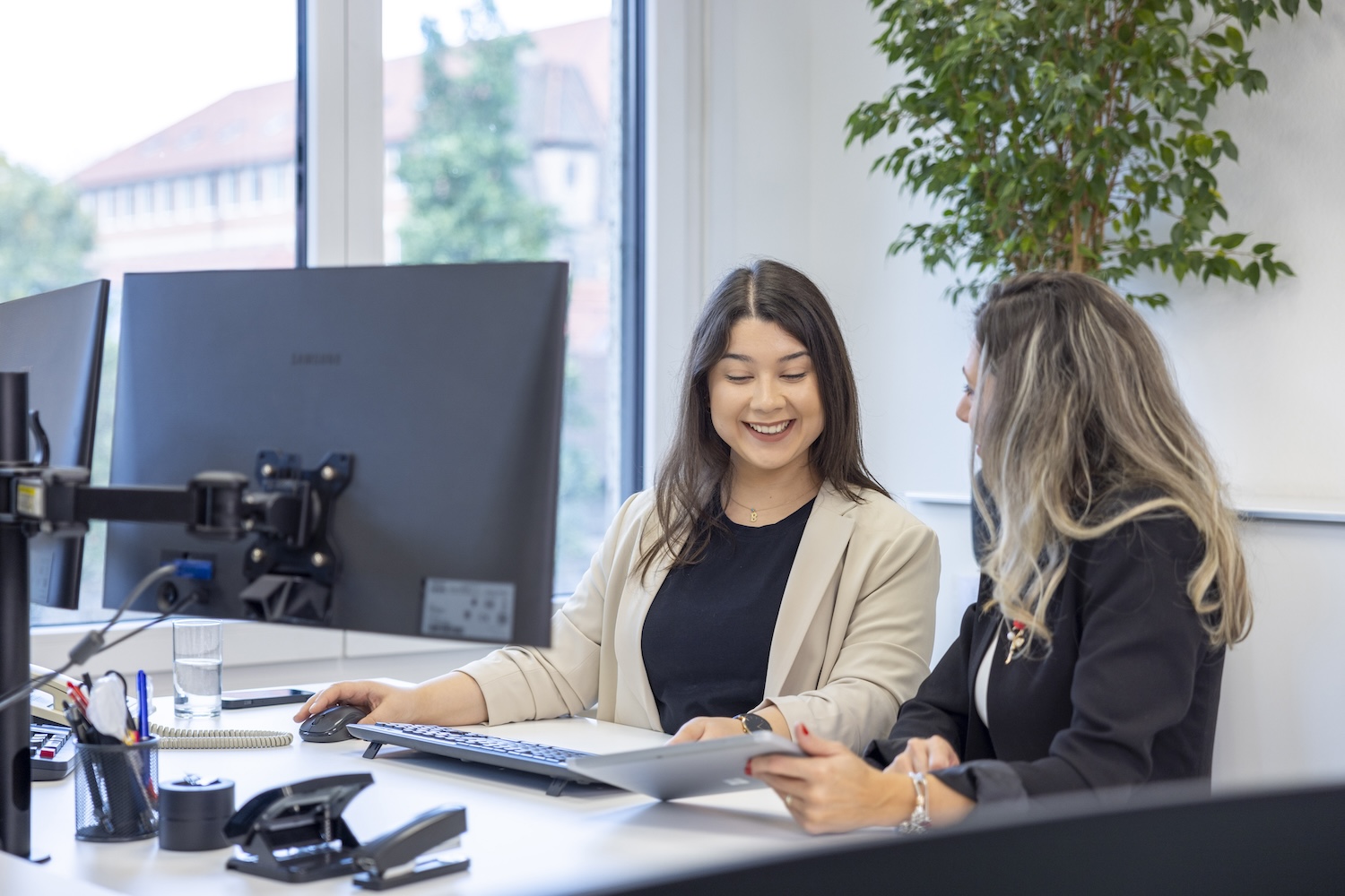 Zwei Mitarbeitende an Schreibtischen mit mehreren Monitoren