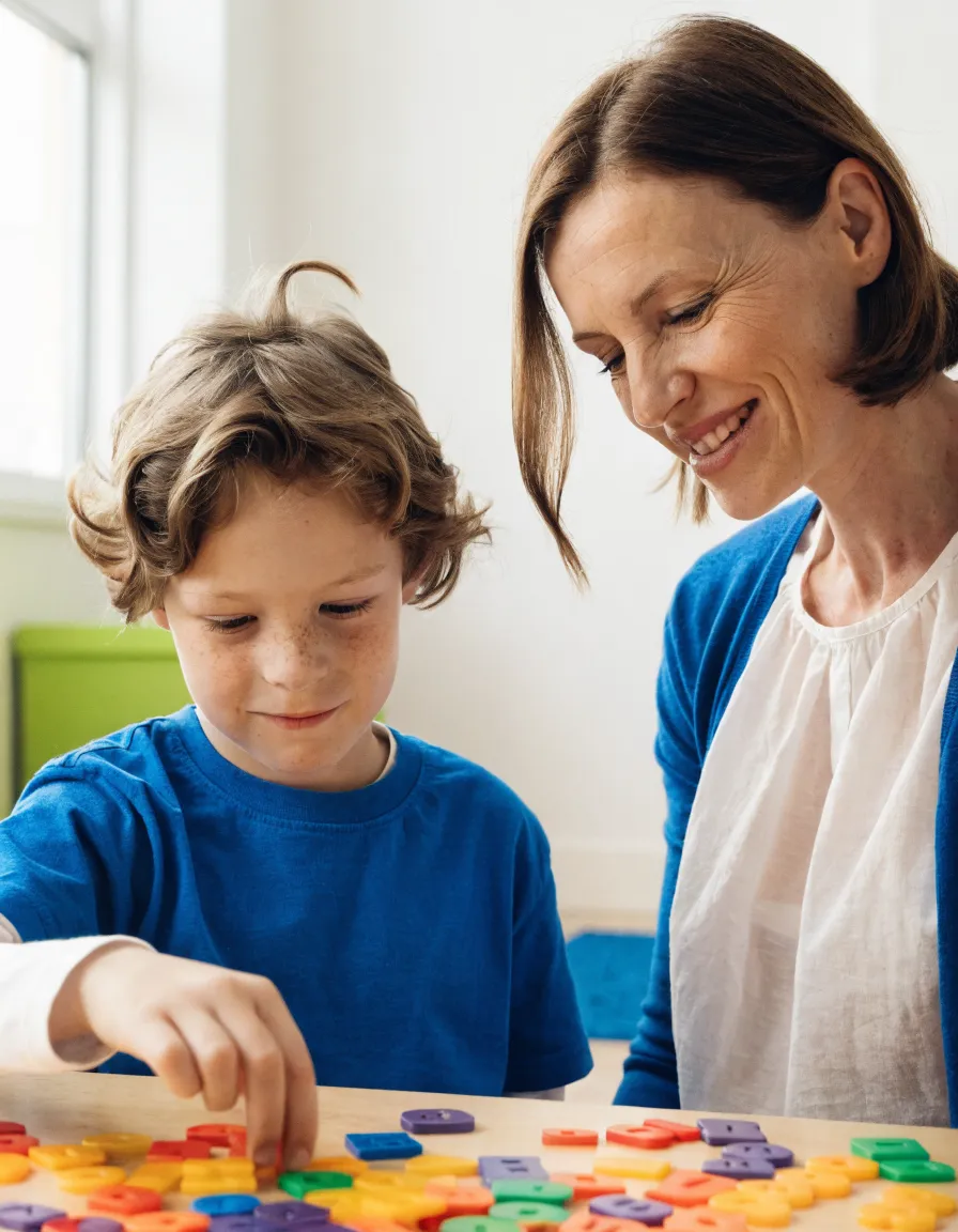 A certified special education teacher working through letter tiles with a young boy at a table