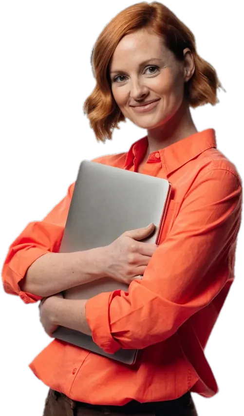 Smiling teacher with red hair in a coral shirt holding a laptop