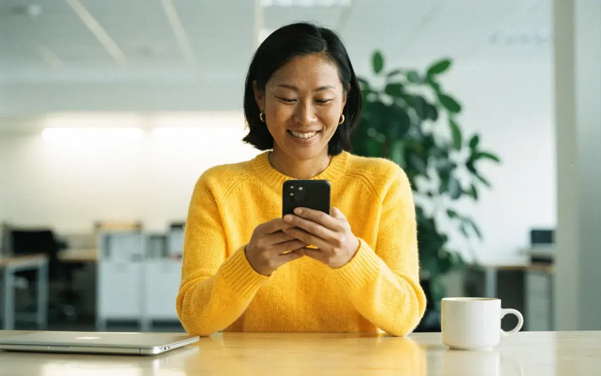 A working parent smiling at her phone at her office desk
