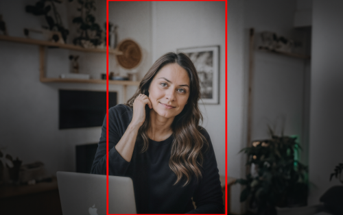 A woman sits in a well-lit room, smiling softly at the camera. She is seated at a desk with a laptop in front of her, exuding a calm and professional demeanor. The background shows a cozy, organized space with minimal decor. This image could represent an educator or professional preparing for a video introduction.