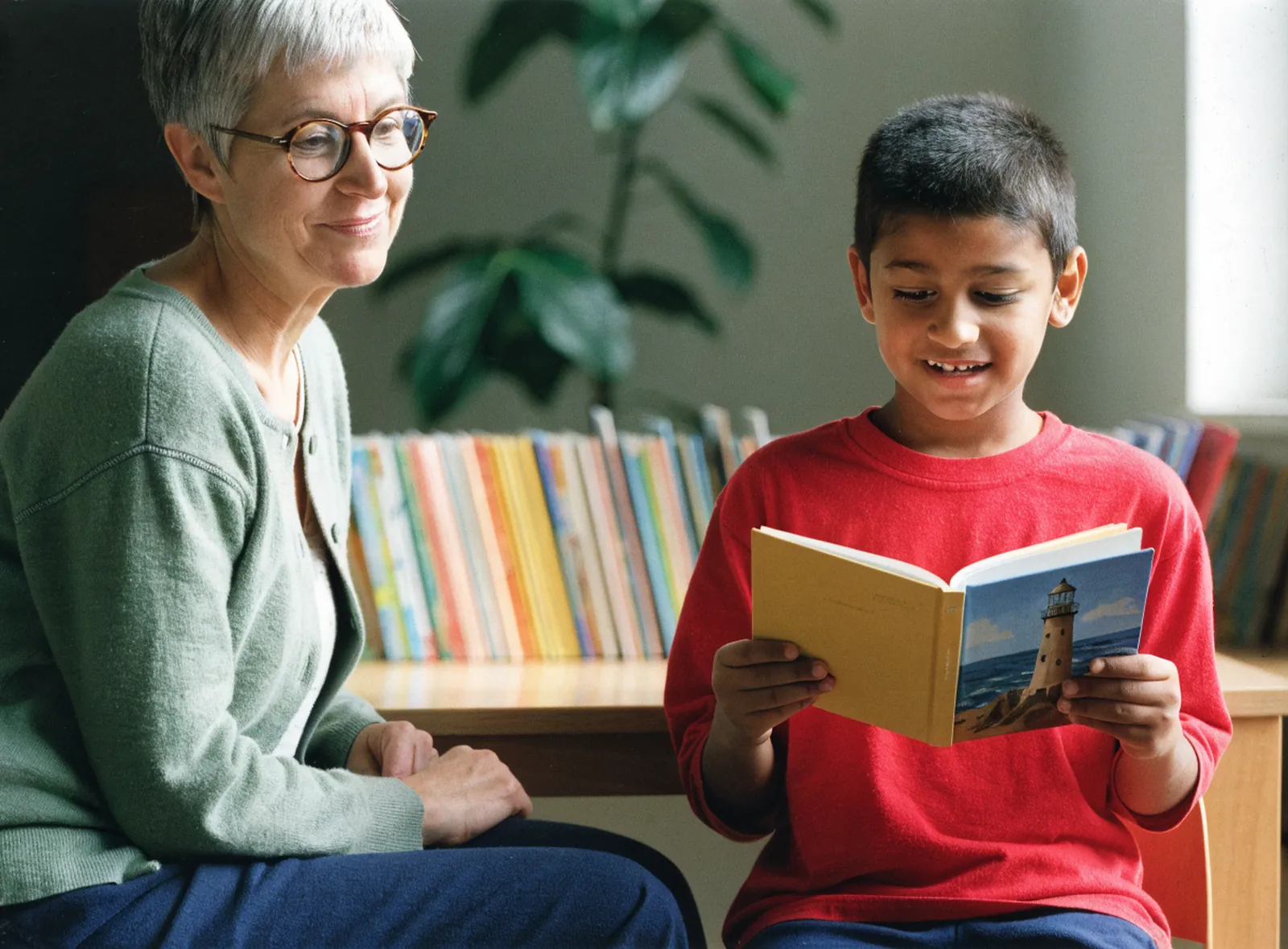 Reading tutor listening as a boy reads a chapter book aloud at the library