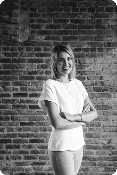 Smiling woman with shoulder-length hair standing with arms crossed in front of a brick wall.