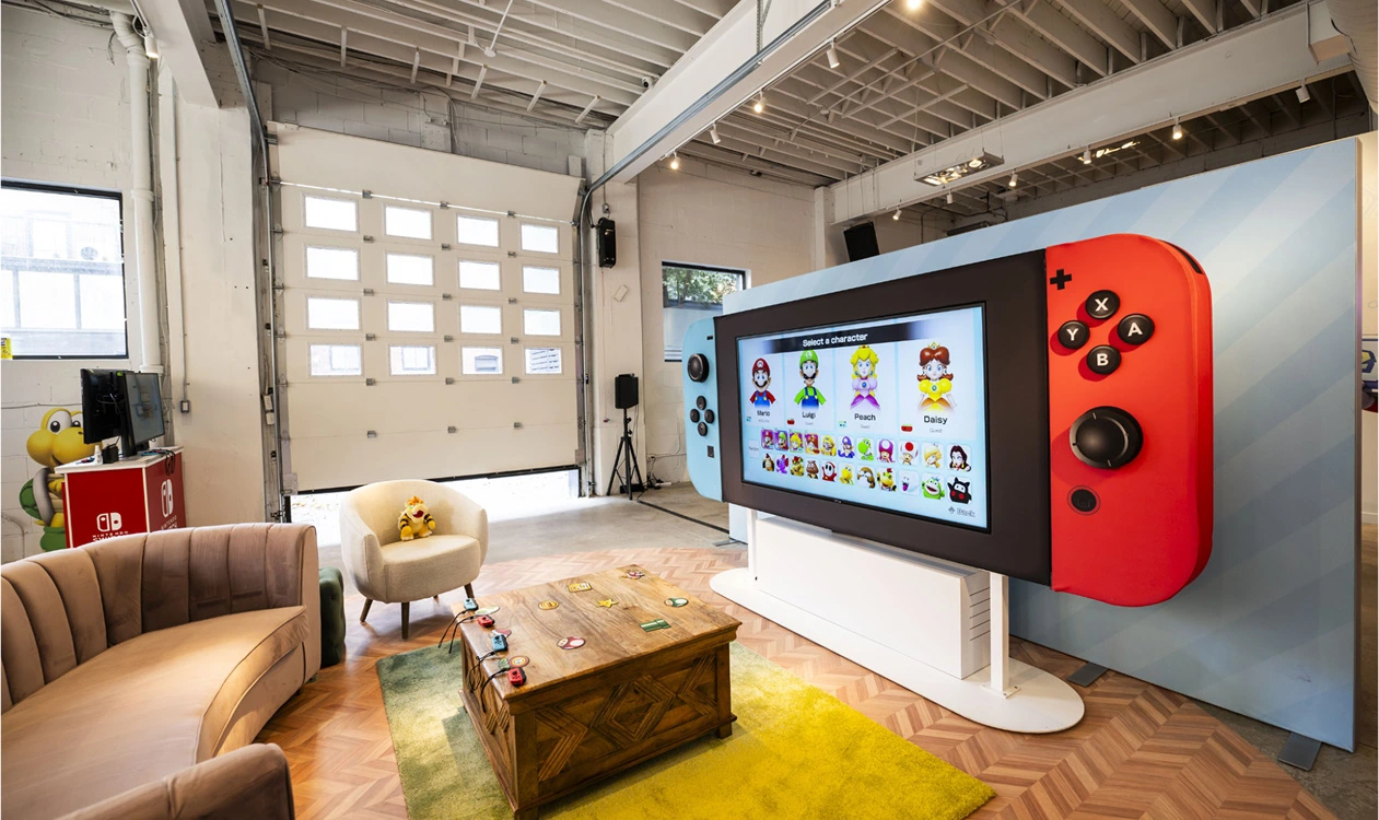 An industrial, loft-like room fitted with a large Nintendo Switch screen, table, and couch. 