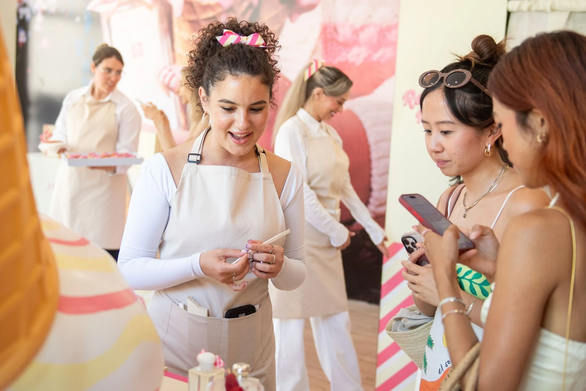 Three women on their phones, taking pictures of items on display at a trade show booth