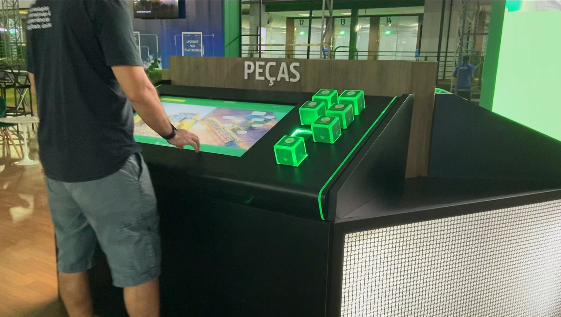 Mesa Cubos da John Deere na Agrishow, com seis cubos acesos em verde no tampo inclinado e um visitante interagindo na tela
