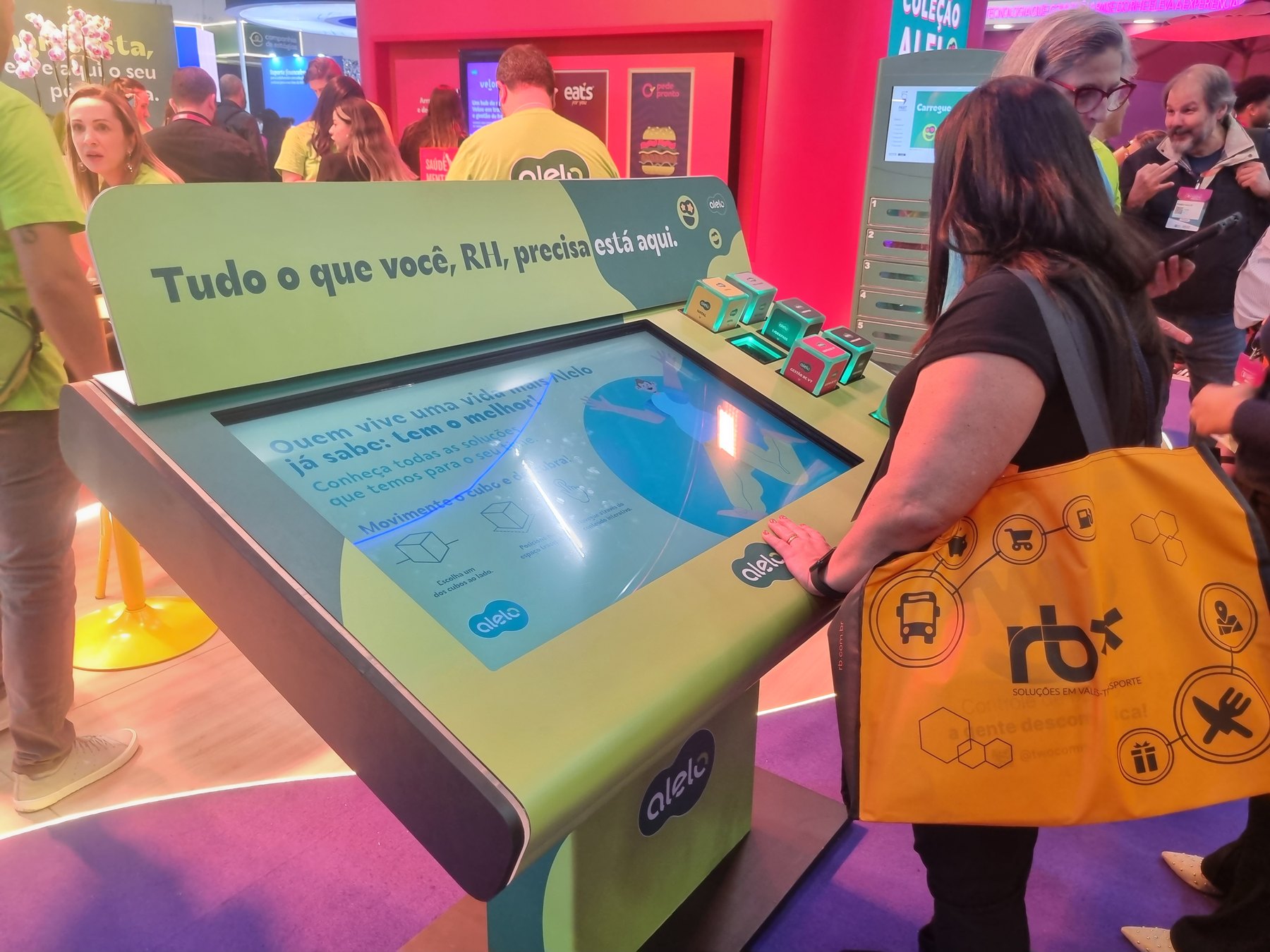 Visitante interagindo na Mesa Cubos da Alelo no CONARH de 2023, com cubos acesos em verde
