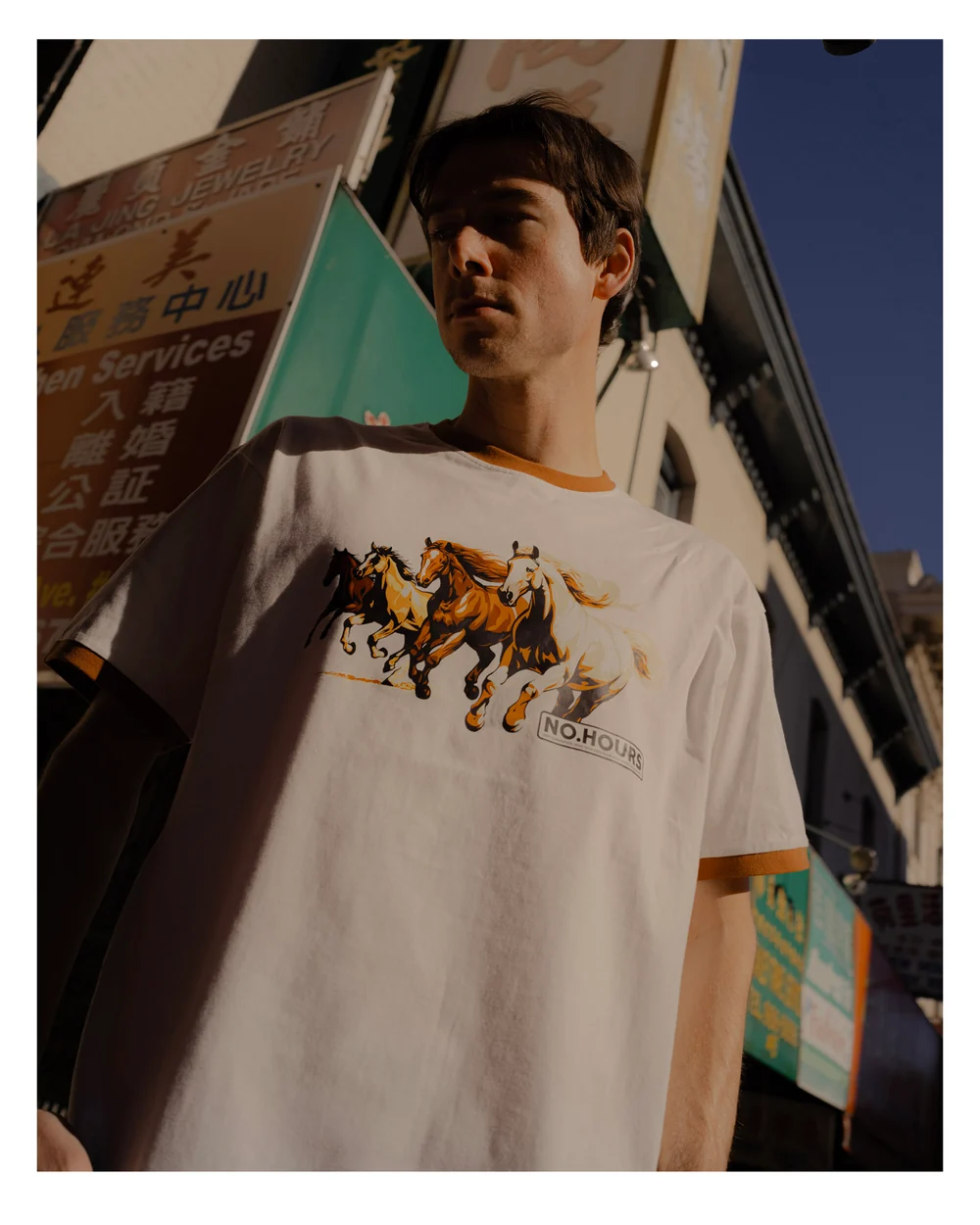 A model wearing a NoHours graphic shirt outdoors.
