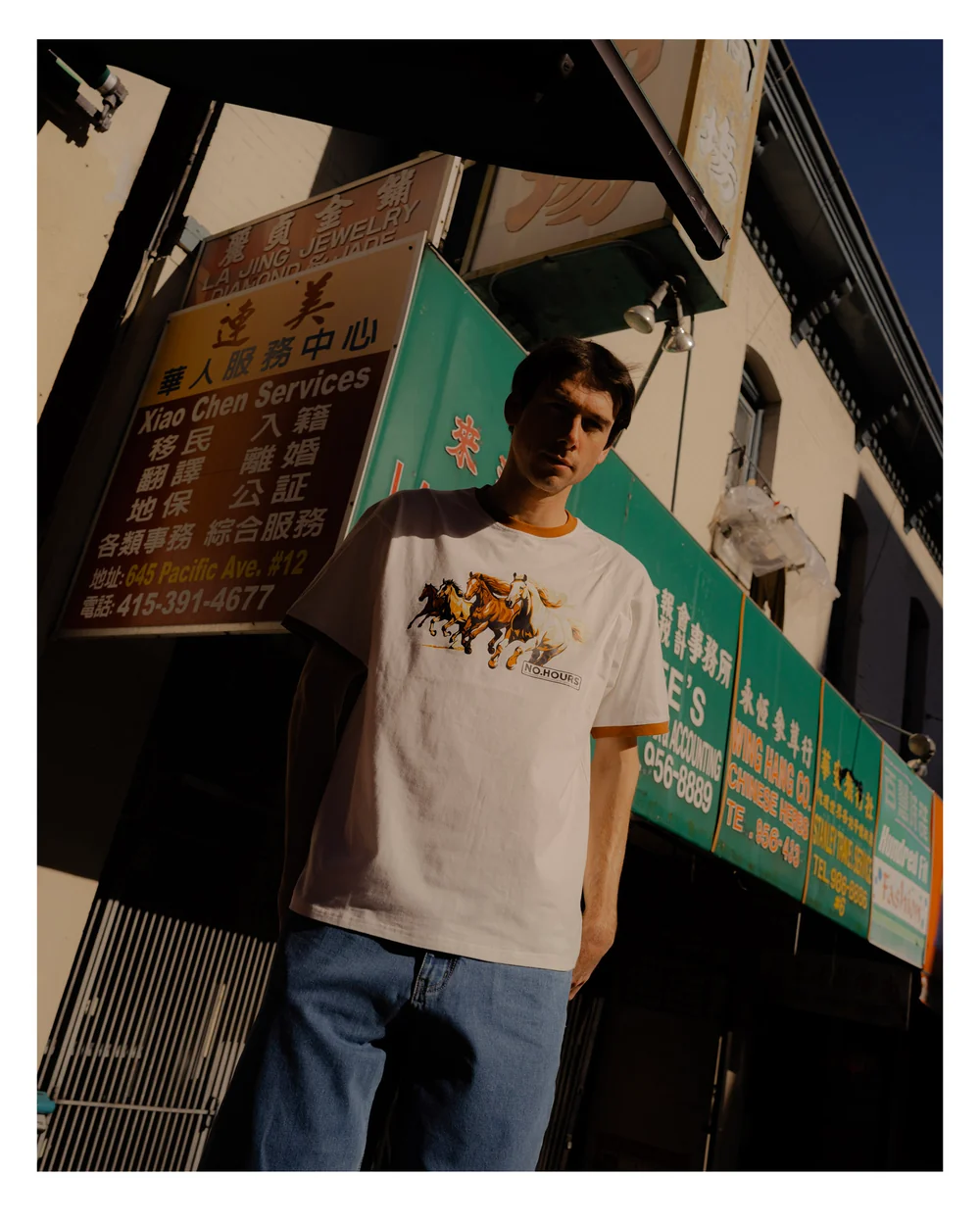 A model wearing a NoHours graphic shirt on a city street in the Spring 25 lookbook.