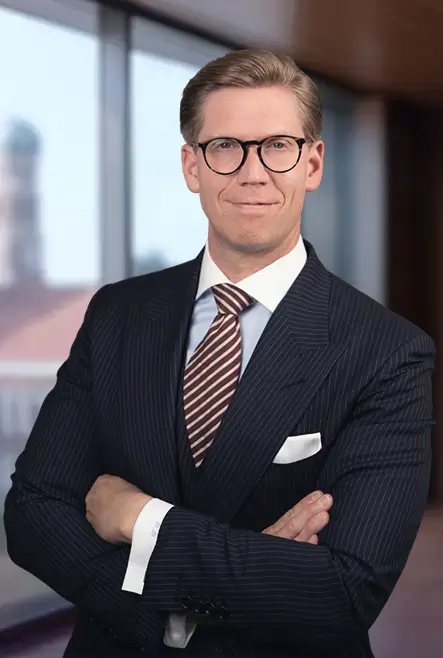 Man wearing glasses in a pinstripe suit and striped tie smiling with arms crossed in an office setting.
