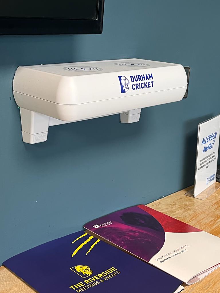 Wall-mounted phone charging shelf in a stadium hospitality environment