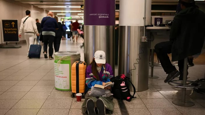 People sitting on floor using wall sockets to charge phones in crowded public space