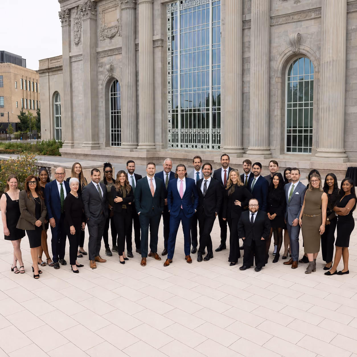 Group of professionally dressed people posing outside a large building with tall windows and columns.