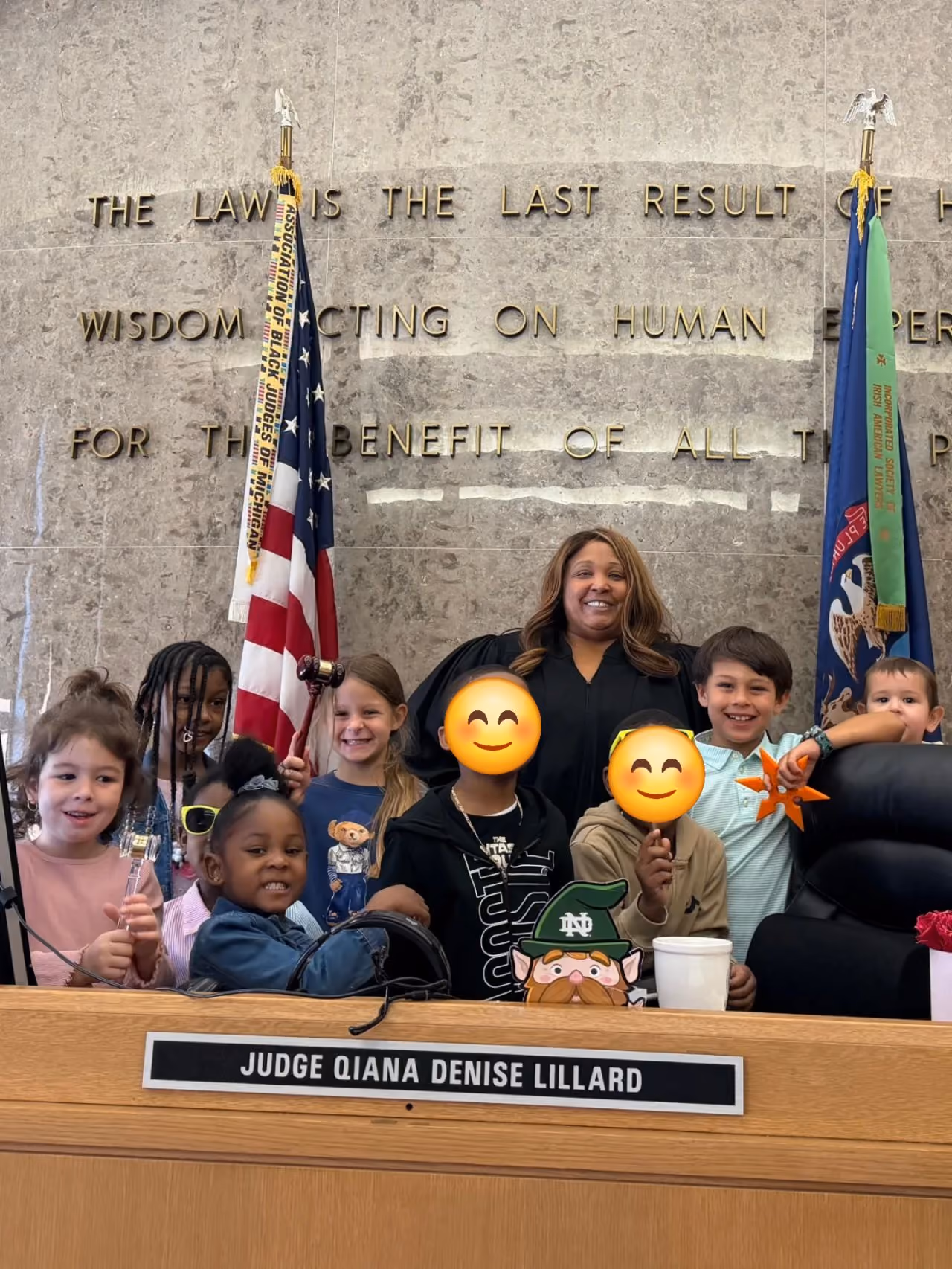 Judge Qiana Denise Lillard smiling with a group of children in a courtroom behind a judge's bench.