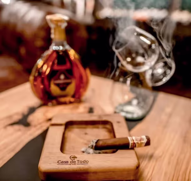 Un pavo y un cenicero con humo, junto a una botella de whisky sobre una mesa de madera.