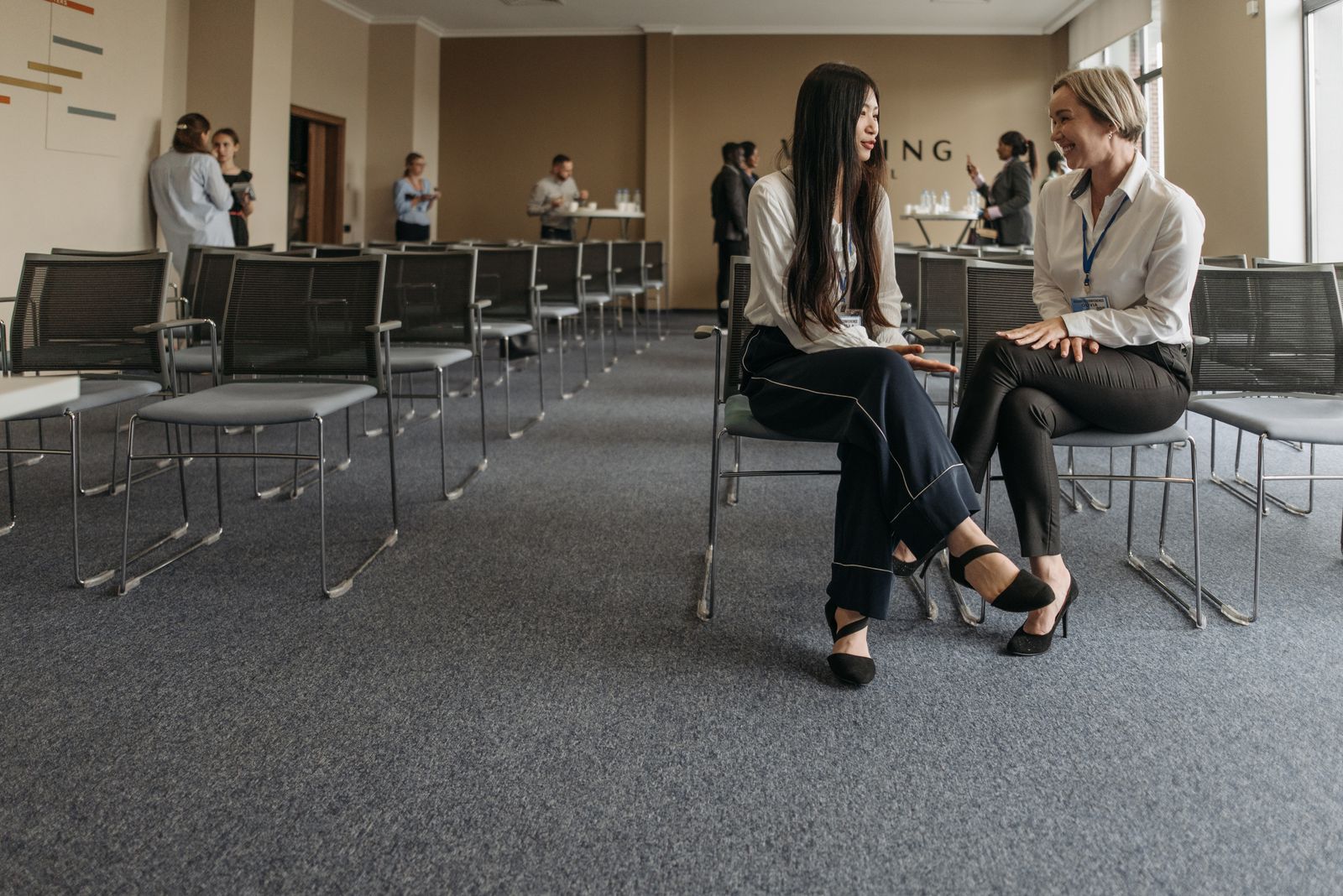 Two professionals talking during a break at a business conference, the kind of event where a marketing team meets people from outside the company