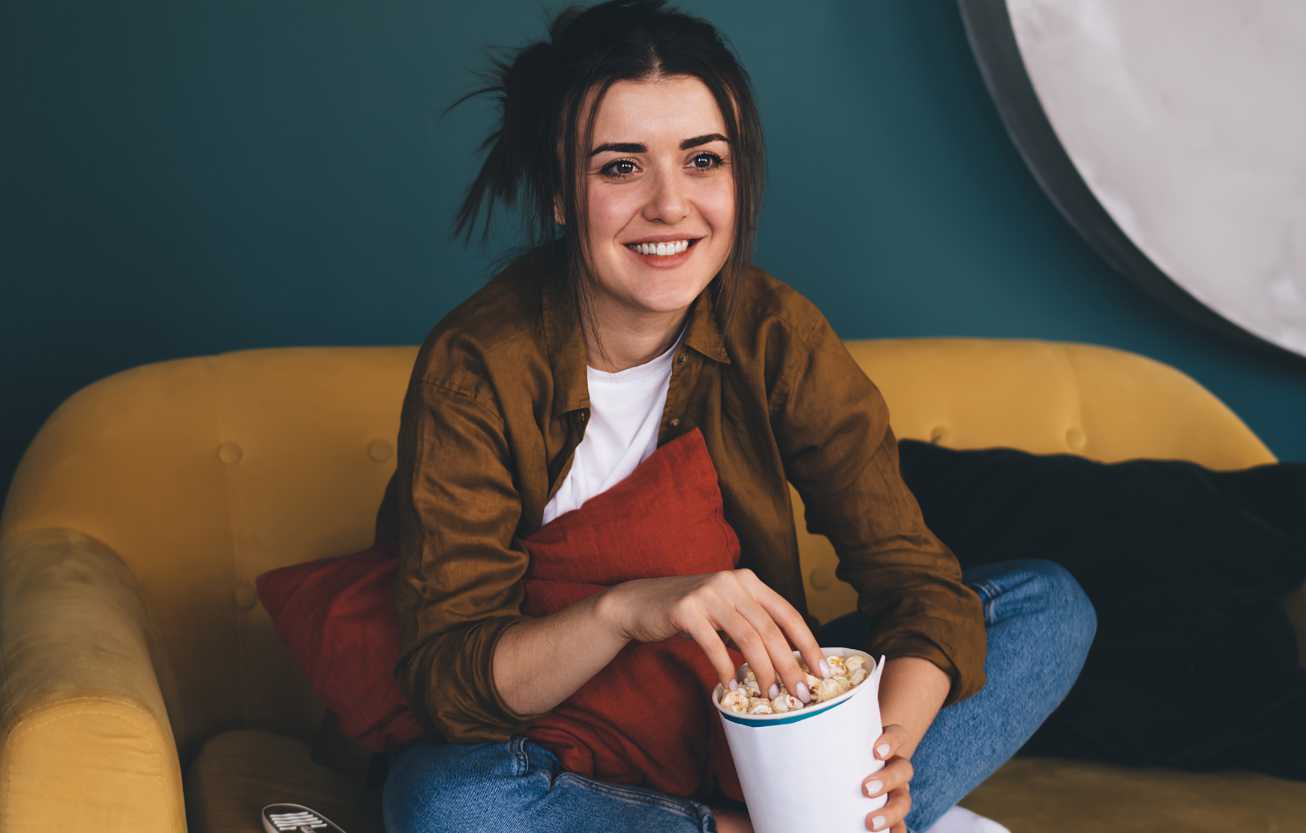 young woman eating popcorn and leaning in to enjoy their television