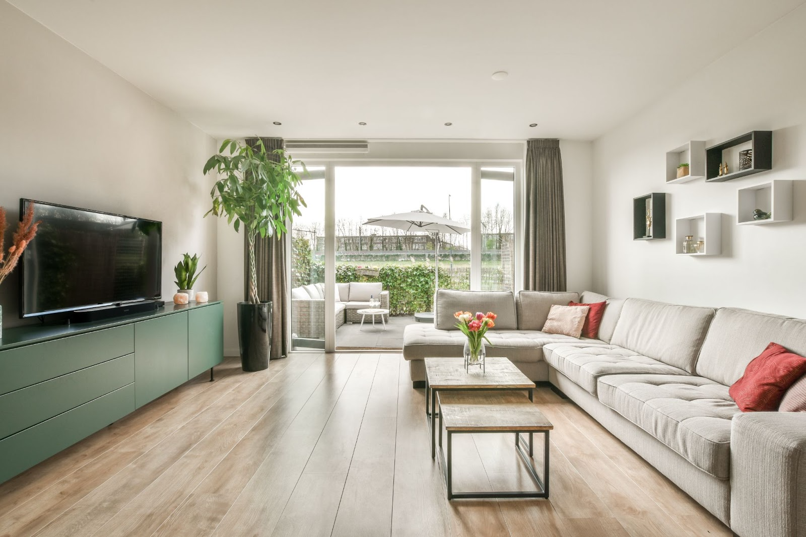 Light and bright living room opening onto an outdoor entertaining area. Cream couch, green entertainment unit, suspended wall shelving, timber floor boards.
