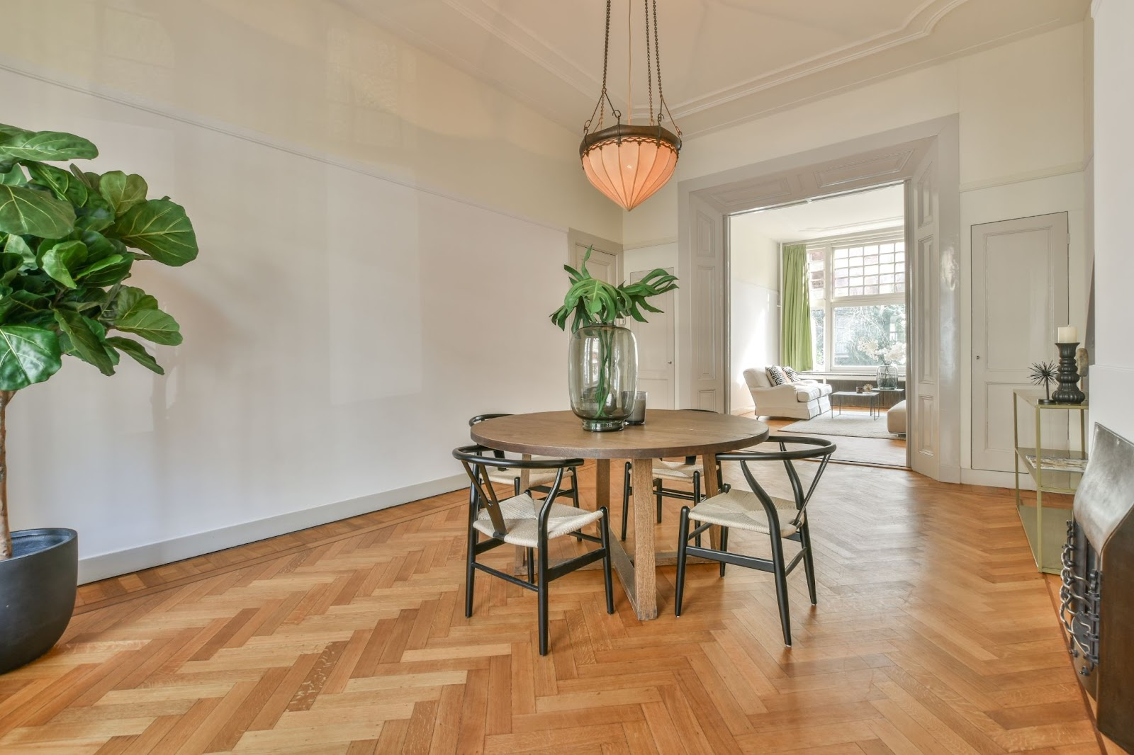 Dining room opening into lounge, herringbone flooring, round timber dining table and chairs, pot plants and an ornate light fitting.