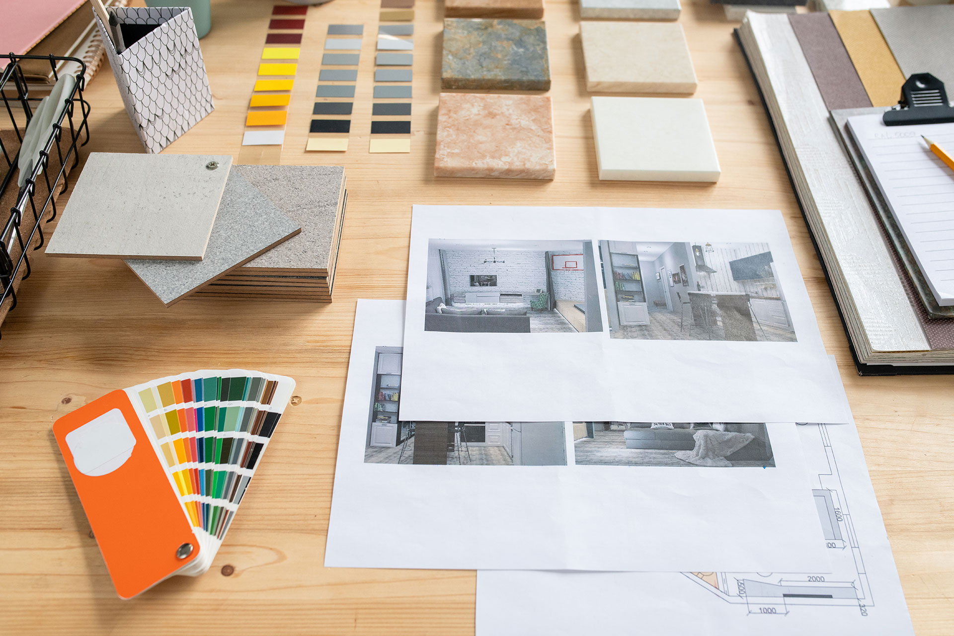 A close-up of a table displays wall paint color charts, tile samples, and printed photos of homes showcasing various flooring styles. The setup suggests interior design planning and material selection.