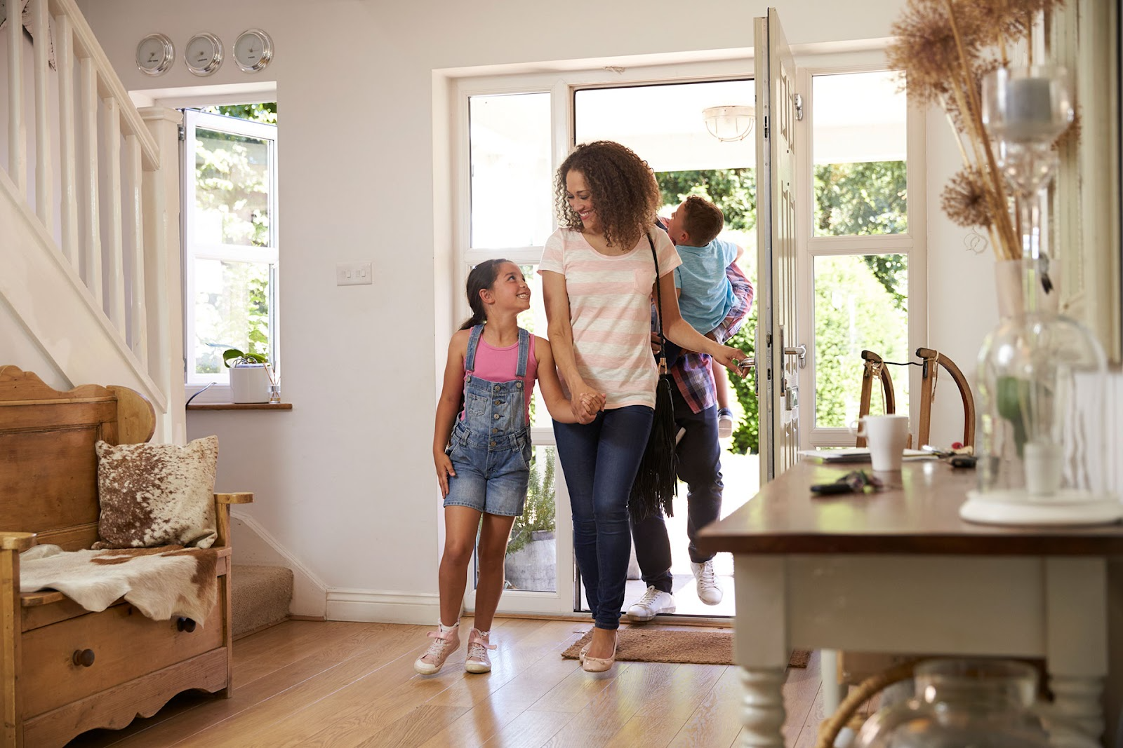 Family coming home - open front door, staircase and open-plan entryway with timber bench seat and side table.