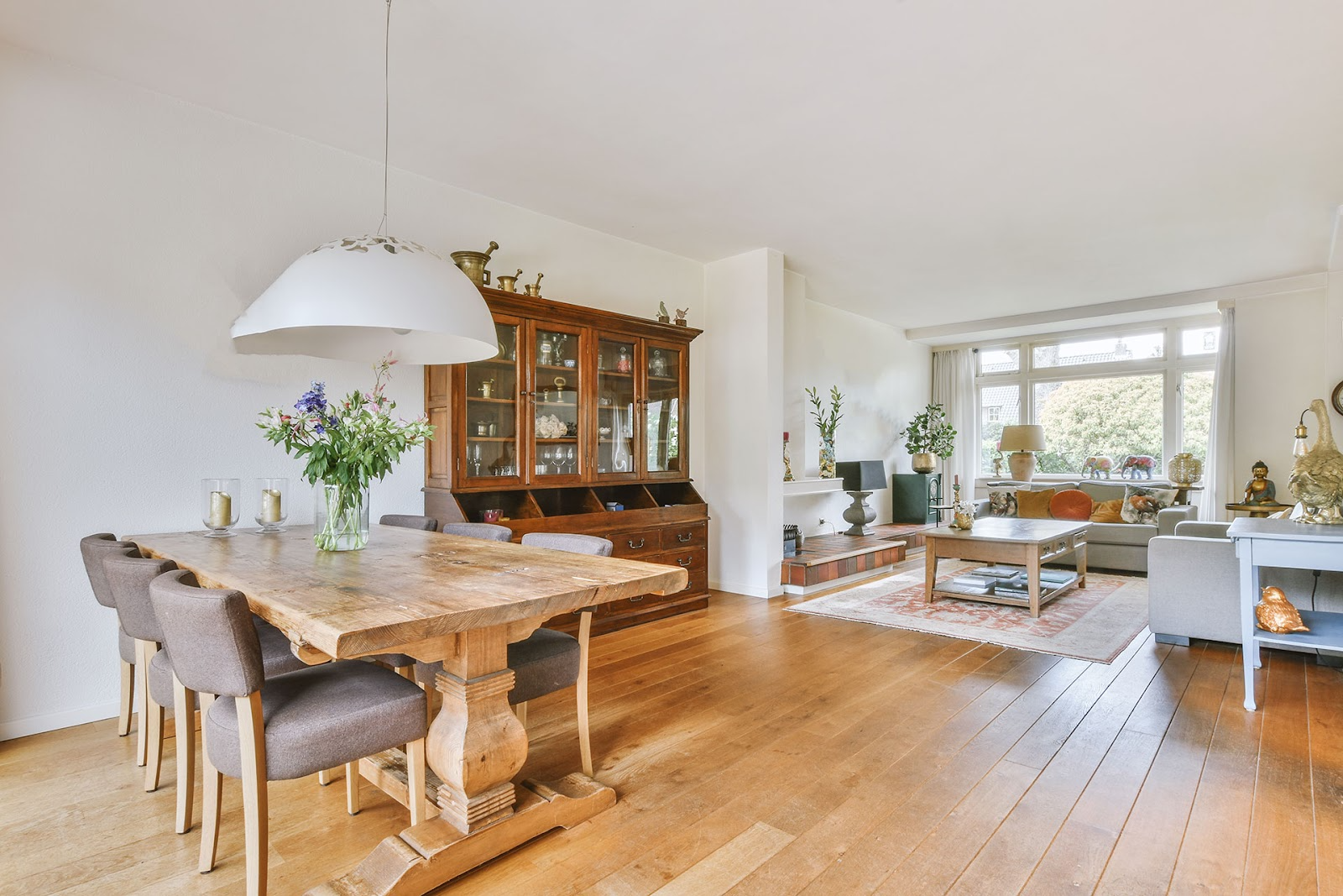 Open-plan country style living/dining area, light coloured lounge setting, rustic timber dining table and buffet, timber floor boards. 
