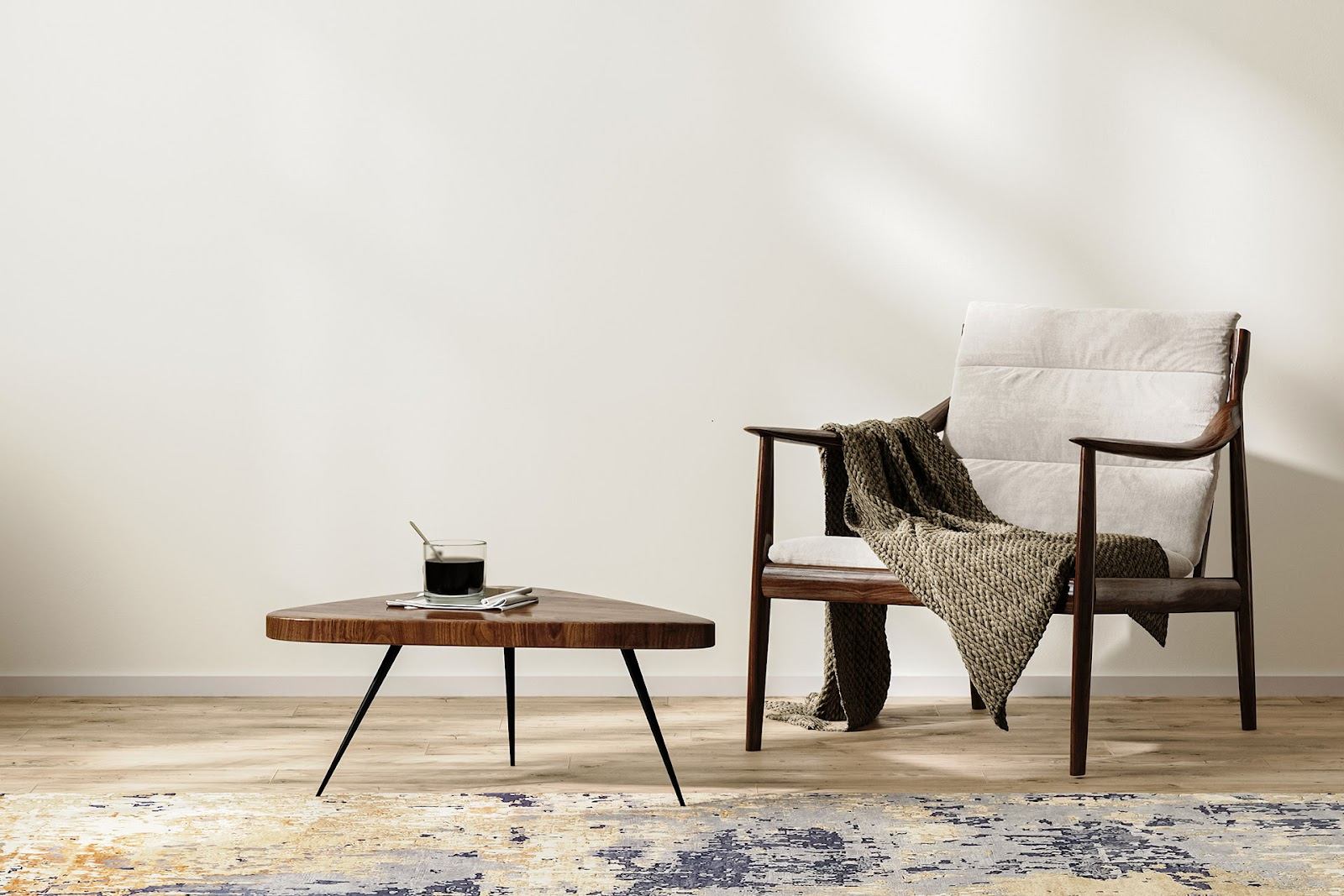 Dark timber and beige occasional chair with green knitted throw rug, triangle timber coffee table, abstract patterned rug and light timber floorboards and off-white walls.
