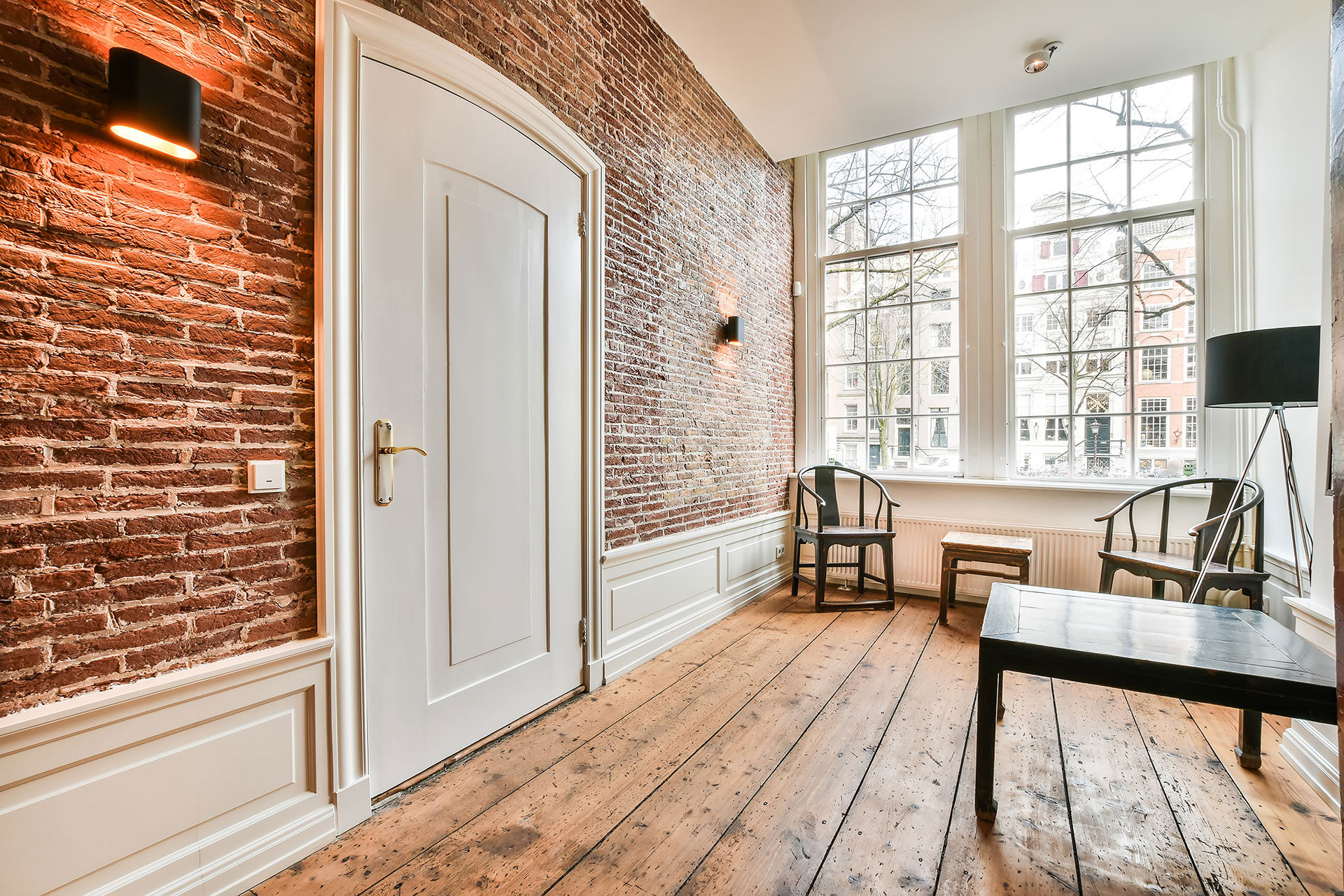An industrial-style interior features rich hardwood flooring and exposed red brick walls. The mix of raw textures and warm wood creates a bold, urban aesthetic.