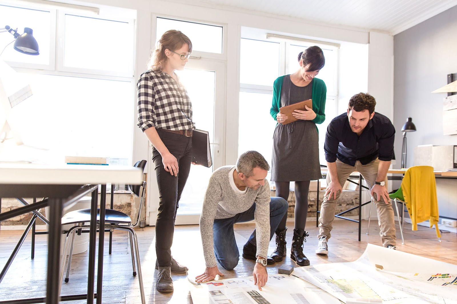 A group of architects bent over a set of plans spread on an office floor.
