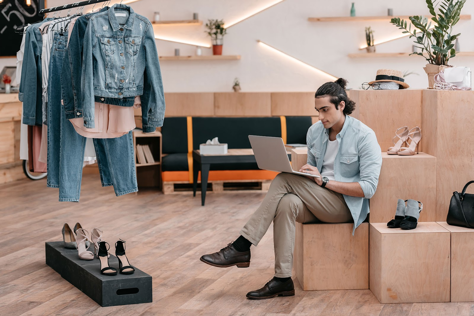 Young man sits with laptop on the floor of a modern clothing store.