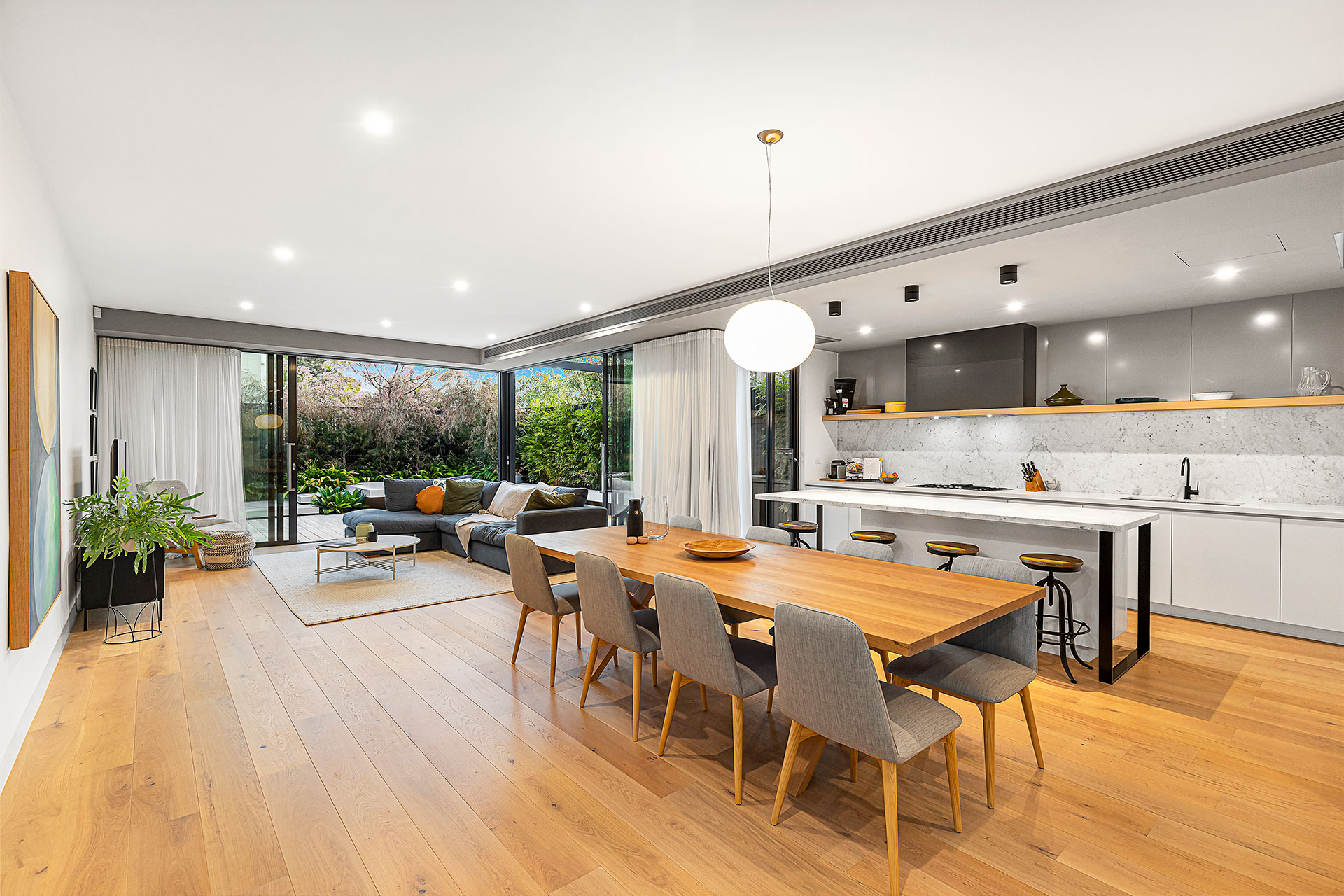 Australian home featuring an open plan kitchen, living area, and dining room with hybrid flooring in a natural wood finish. Seamless layout enhances flow and modern aesthetic.