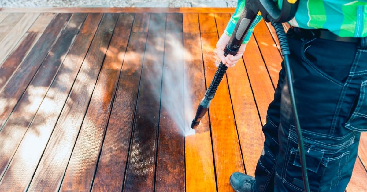 power washing - man cleaning terrace with a power washer - high water pressure cleaner on wooden terrace surface