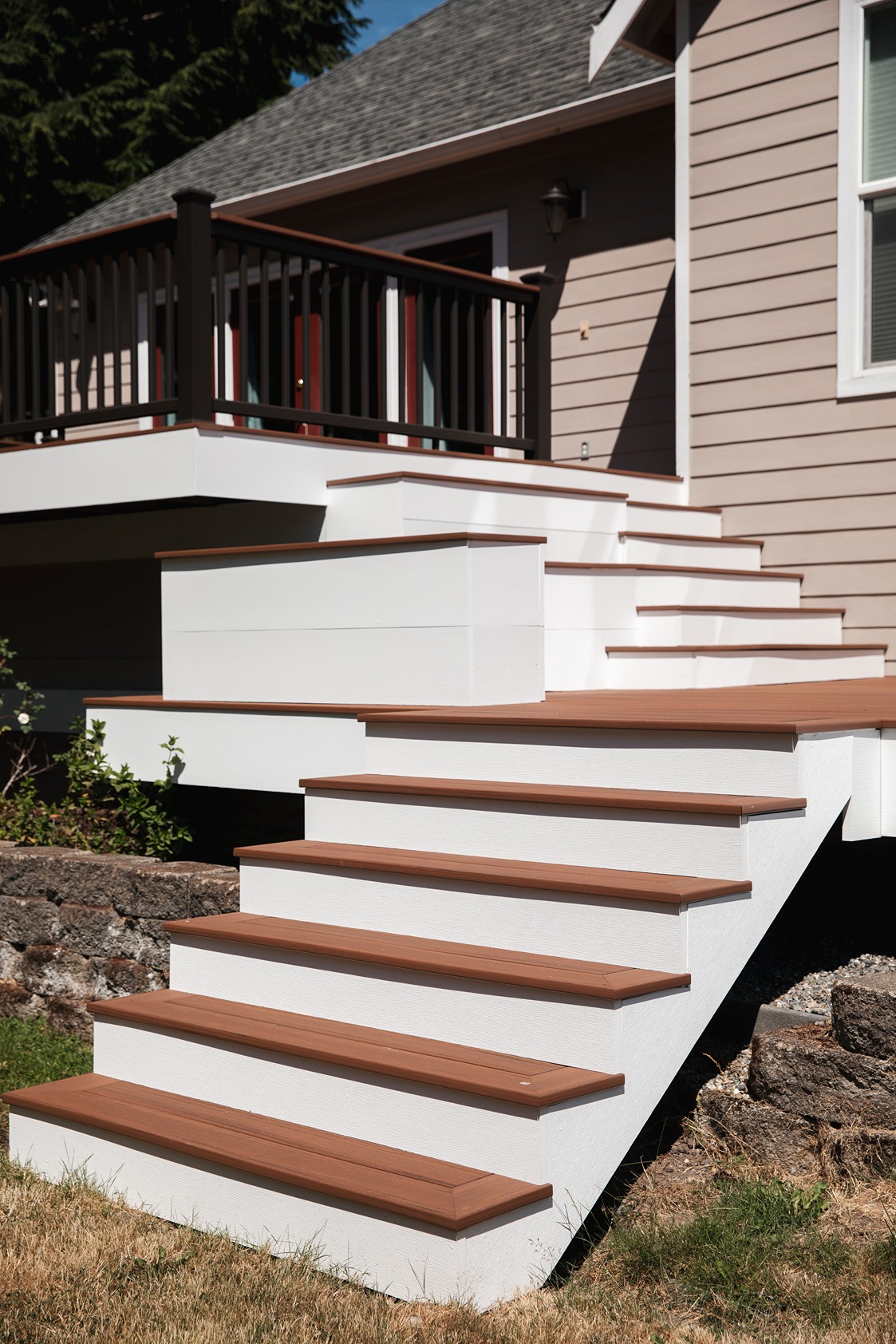 Brown composite deck stairs with white risers and picture-frame treads, leading to an upper deck with black railing