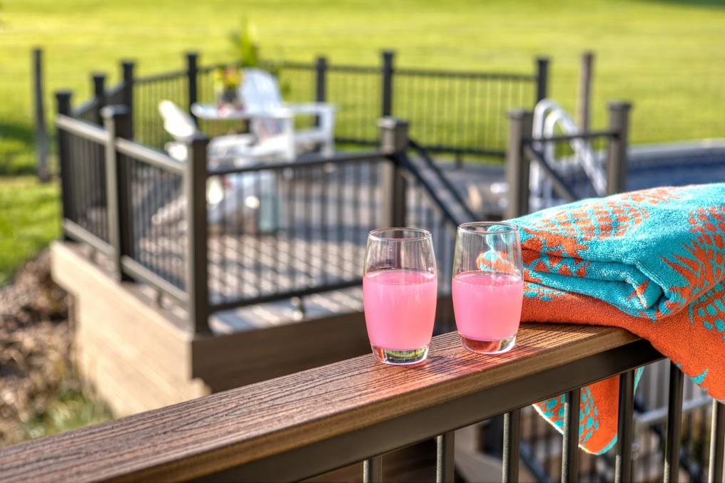 Cocktail drink rail on black aluminum deck railing with composite wood cap, two pink drinks and towel by a backyard pool