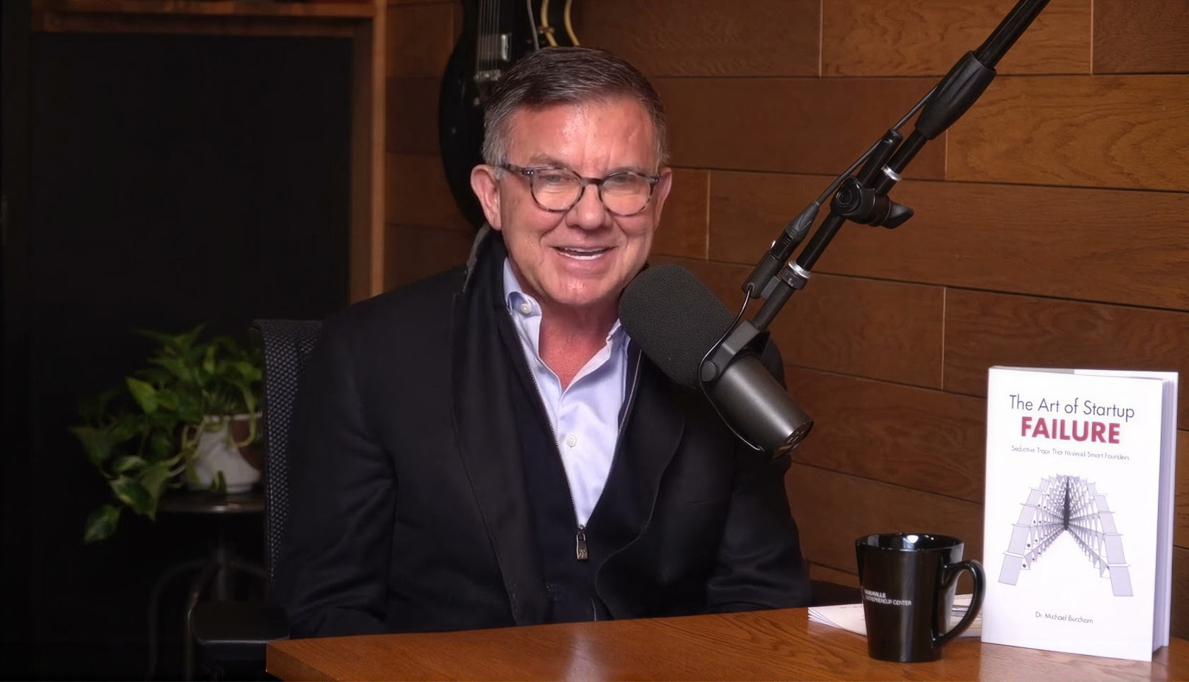 Michael Burcham at a podcast microphone, with a copy of The Art of Startup Failure