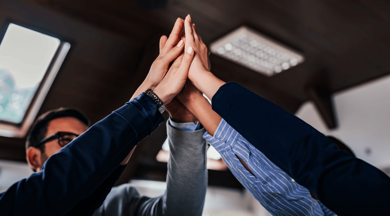 Four people in business attire giving a group high-five indoors.