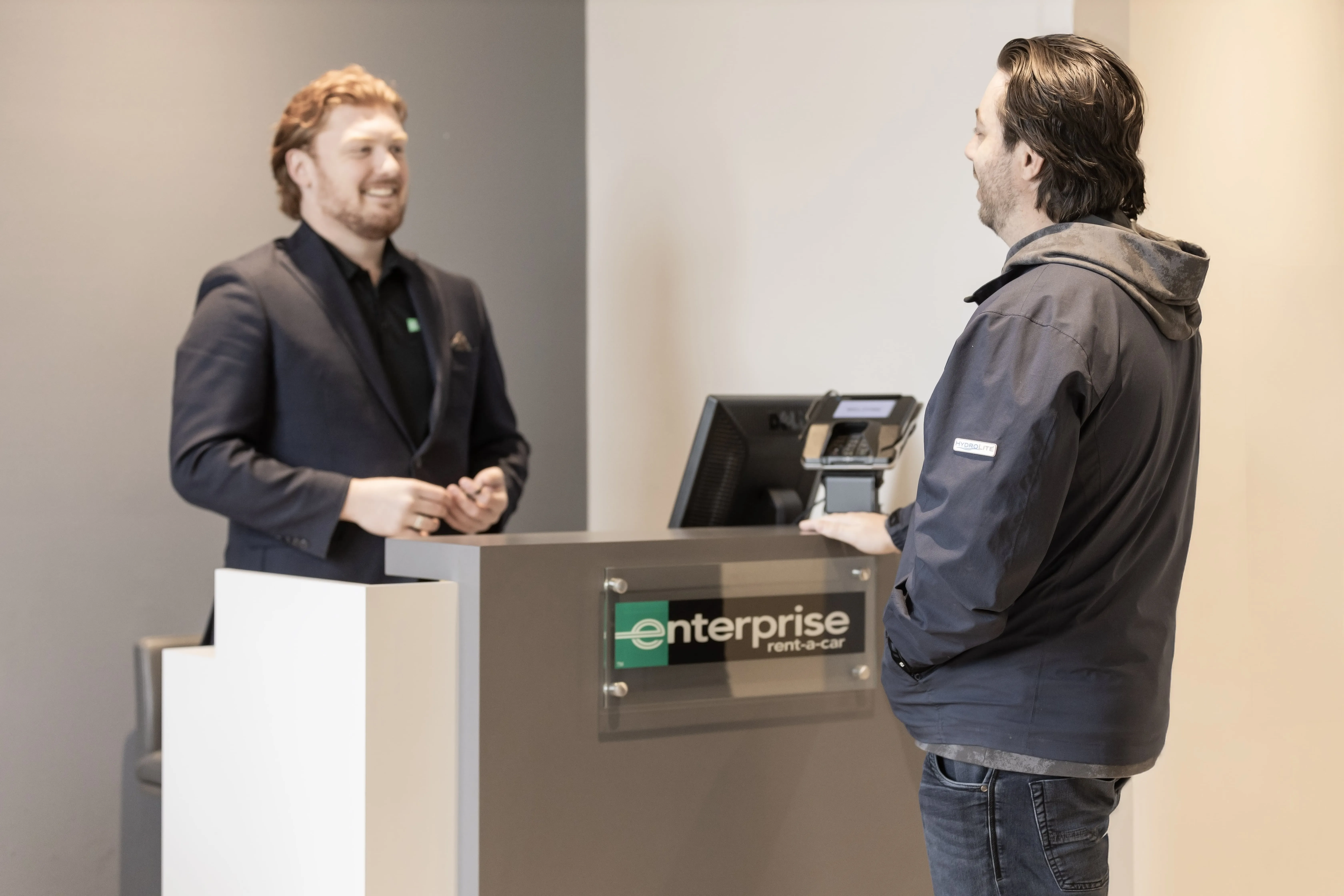 Desk with “Enterprise” signage and have a person handing keys to another person