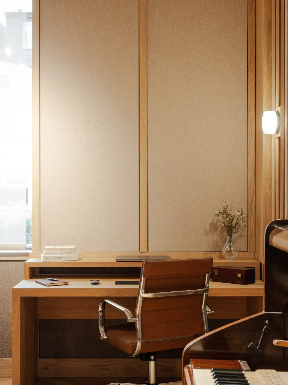 A stylish studio for composing music featuring wood and fabric sound proofed walls, herringbone flooring, pianos and a minimalistic desk