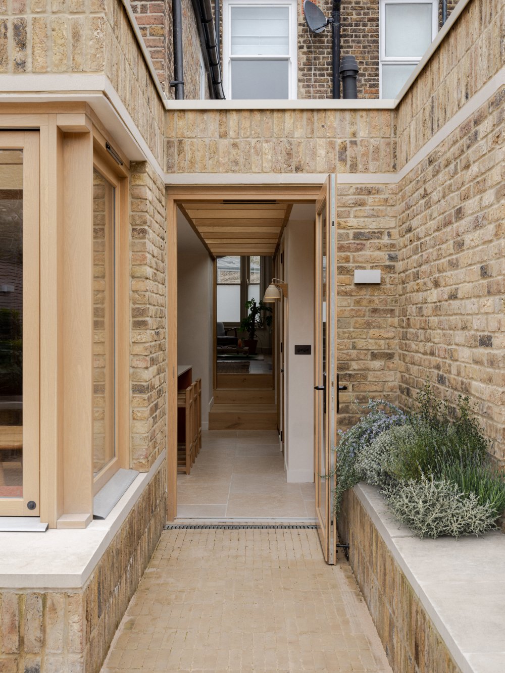 Exterior view of the Strata House limestone brick extension, highlighting an oak-framed side door to the garden by London architects Benjamin Wilkes.