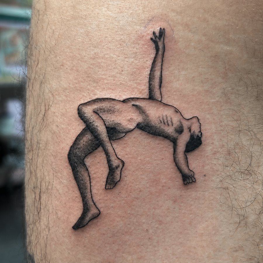 Surreal black-and-grey crouching figure with a raised arm on a leg tattoo